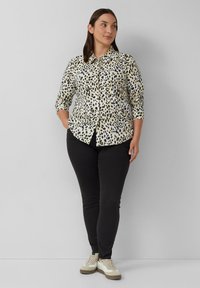 Lange mouw overhemd in een licht crèmekleurige stof met een zwart luipaardprint, gecombineerd met zwarte slim-fit broek en witte sneakers.