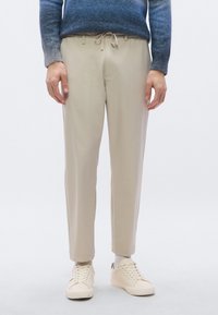 Beiget, kapealahkeiset housut, joissa on joustava vyötärönauha ja kiristysnauha. Sileä kangaspinta, ei näkyviä kuvioita. Yhdistetty valkoisiin lenkkareihin.