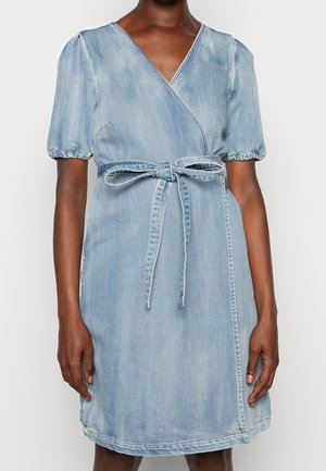 Light blue denim wrap dress with short puff sleeves and a tied belt at the waist worn by a dark-skinned person against a white background.