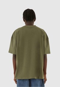 Olivenfarvet oversized T-shirt, korte ærmer, rund hals, lavet af blødt stof, glat tekstur, ingen synlige mønstre eller hardware.