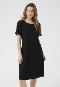 Black linen dress with a round neckline, short sleeves, relaxed fit, and side pockets, extending to just below the knee. Smooth texture.