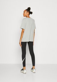 Camiseta de algodón gris con un corte holgado, combinada con leggings negros que tienen un acento blanco curvado y zapatillas gris con un acabado texturizado.