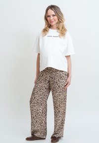 Vit t-shirt med texten "COOL MAMA", kombinerad med löst sittande, tan leopardmönstrade byxor och bruna slip-on skor. Mjuk tyg och avslappnad design.