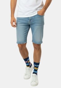 Pantalones cortos de mezclilla azul claro con corte recto y dobladillo deshilachado, combinados con calcetines estampados y zapatillas blancas. La camiseta es blanca lisa.