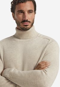 Beige Rollkragenpullover aus Strickstoff. Merkmale sind der gerippte Kragen und die Bündchen, mit einer strukturierten Oberfläche und weiten Ärmeln.