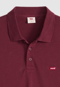Burgundy színű pólóing, textúrázott anyagból, három gombos kivágással és egy kis piros Levi's logóval a mellkasán. Hagyományos szabású.