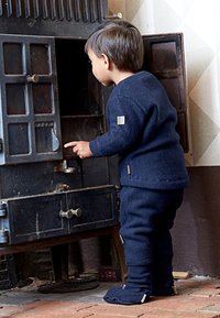 Temno modra volnena obleka za otroka, ki vključuje pulover s čoln izrezom in oprijete hlače. Otroške nogavične nogavice, ki se ujemajo z obleko, imajo majhne etikete.