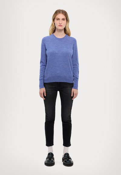 Pull bleu à manches longues en tricot doux, col rond, associé à un jean slim noir et des chaussures à plateforme noires. Tissu simple et texturé sans motifs.