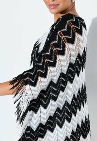 Svart och vit plädmönstrad stickad poncho med fransdetaljer, med öppet stickdesign och lös form för en avslappnad passform.