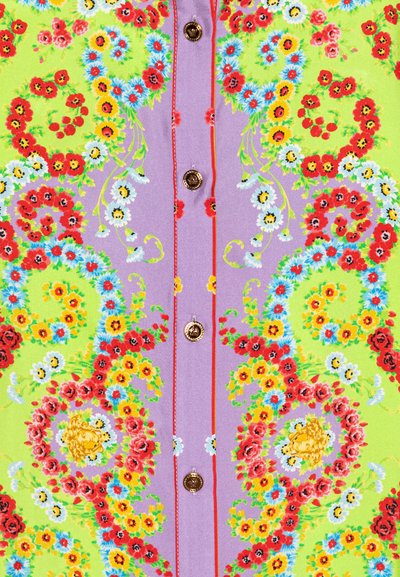 Tela con patrón floral que presenta flores brillantes en rojo, amarillo y azul sobre un fondo verde y morado, con botones dorados y costuras rojas.