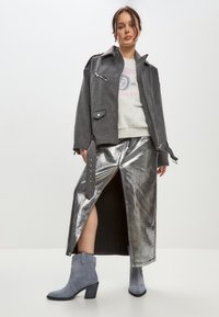 Chaqueta de mezcla de lana gris con cremalleras, falda maxi plateada metálica con una abertura lateral y botas de ante azules hasta el tobillo con un tacón grueso.