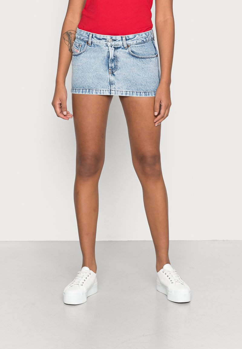 Jeansminikjol i ljusblått, med en figurnära design, fem-fickorsstil och kontrasterande sömmar. Kombinerad med vita sneakers och en röd topp.