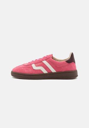 Pink suede sneakers with white stripes and a brown rubber sole. Rounded toe, flat laces, and padded ankle detail. Brand logo on side.