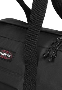 Zwarte duffeltas met duurzaam stof, brede geweven riemen en een ritssluiting aan de bovenkant. Met het Eastpak-logo en trekkoorddetails. Soepele textuur.