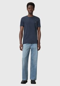 Námořnické tričko s krátkým rukávem z měkkého materiálu, v kombinaci s světlými modrými širokými džíny a černými botami. Jednoduchý design s minimálními akcenty.