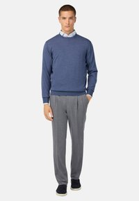 Moška modra pletena majica z okroglim izrezom, v kombinaciji s sivimi nabranimi hlačami. Obleka vključuje svetlo modro srajco s kragnjo pod njo.