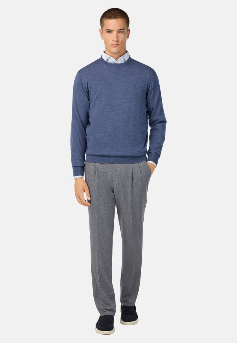 Moška modra pletena majica z okroglim izrezom, v kombinaciji s sivimi nabranimi hlačami. Obleka vključuje svetlo modro srajco s kragnjo pod njo.