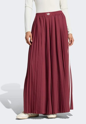 Lunga gonna plissettata bordeaux con logo Adidas in vita, indossata con top bianco e sneakers bianche.