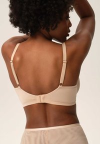 Beżowy biustonosz widoczny z tyłu, z regulowanymi ramiączkami i zapięciem na haftkę. Gładka tekstura tkaniny o minimalistycznym designie.