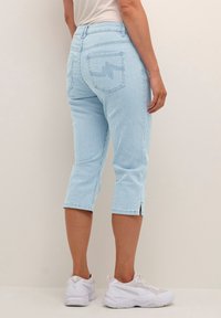 Světle modré krátké kalhoty s vertikálním pruhovaným vzorem, s zipem na lemu a dvěma zadními kapsami. Nosené s bílými teniskami.