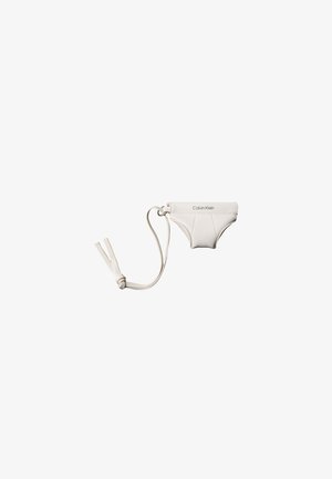 Kleine weiße Calvin Klein Tasche in Form von Unterwäsche mit Handgelenksriemen und Knoten auf schlichtem weißen Hintergrund.