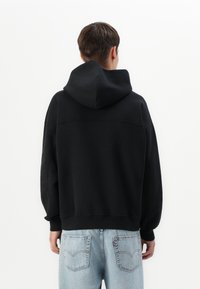 Sweatshirt à capuche noir avec une coupe décontractée. Caractéristiques : poignets et ourlet côtelés, texture lisse et design simple. Porté avec un jean bleu clair.