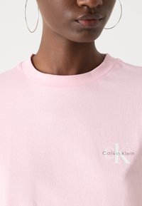 Light pink cotton t-shirt featuring a crew neck, short sleeves, and a white "Calvin Klein" logo on the left side.