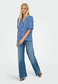 Blå blomsterbluse med pufærmer, parret med lyseblå flared jeans. Outfittet har en v-udsagnsdesign og kraftige hæle.