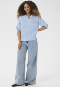 Blouse bleu clair à manches courtes avec un col en V et des manches retroussées, assortie à un jean en denim clair à jambes larges et des chaussures plates noires avec des accents.