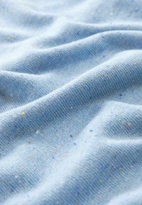 Tissu tricoté bleu clair avec une texture lisse, comportant de petites taches vertes, jaunes et orange réparties sur toute la surface.