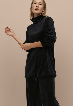 Top in velluto nero con colletto alto, maniche lunghe e orlo regolabile con cordino. Presenta una vestibilità comoda e una texture liscia e morbida.