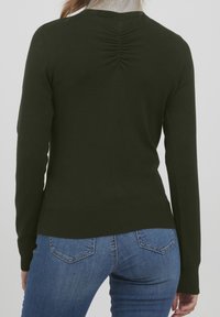 Tmavě zelený přiléhavý svetr s kulatým výstřihem, dlouhými rukávy a shromážděným detailem na zádech. Žebrované manžety a spodní lem. V kombinaci s modrými džínami.