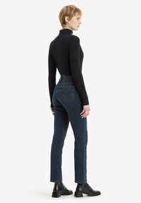 Zwarte geribbelde lange mouwtop gecombineerd met hoge, donkerblauwe jeans en zwarte enkellaarsjes met hak. De outfit heeft een getailleerde silhouet.