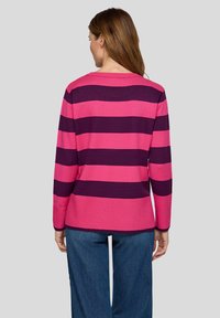 Fuchsia- und dunkelviolett gestreifter Pullover mit langen Ärmeln, einem Rundhalsausschnitt und einem gerippten Saum, kombiniert mit Jeanshosen.