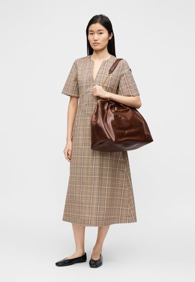 Καφέ καρό midi φόρεμα με κοντά μανίκια και V-λαιμόκοψη, σε συνδυασμό με μια σκούρα καφέ δερμάτινη χαλαρή τσάντα ώμου με χρυσή αλυσίδα.