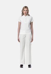 Polo bianco con colletto, abbinato a pantaloni bianchi a gamba larga. L'outfit presenta una texture liscia e un design minimalista.