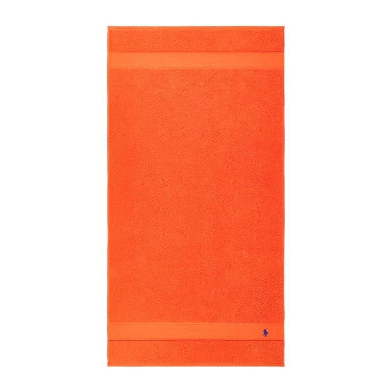 Πορτοκαλί πετσέτα από περκάλι με υφή, με μονόχρωμο σχεδιασμό και δύο οριζόντιες ρίγες κοντά στην κορυφή. Περιλαμβάνει ένα μικρό λογότυπο.
