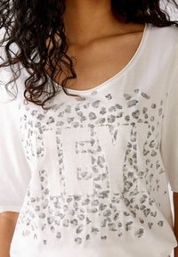 Witte korte mouw top met een "HEY!" grafiek in zilveren luipaardprint en versieringen, met een ontspannen pasvorm en zachte textuur.