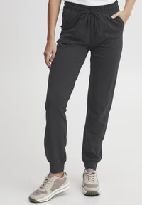 Svart joggebukser med elastisk midje, snøring, sidelommer og smalnette mansjetter. Laget av glatt, lett materiale.