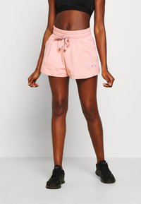 Světle růžové sportovní šortky s elastickým pasem a stahovací šňůrkou. Mají boční kapsy a vyšitý logo na lemu.