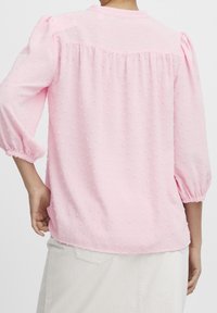 Blusa rosa con un motivo strutturato, maniche a sbuffo a tre quarti e scollo rotondo. Presenta un pannello posteriore arricciato e polsini elastici.