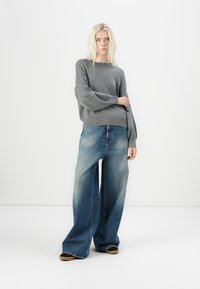 Lichtgrijze gebreide trui met brede mouwen, gecombineerd met oversized blauwe denim jeans met een vervaagde wassing en een ontspannen pasvorm.