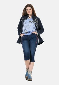 Granatowa kurtka z kwiatowymi haftami, jasnoniebieska koszulka z grafiką, ciemnoniebieskie capri z kwiatowymi akcentami oraz metaliczne botki za kostkę.