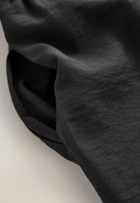 Gros plan sur un tissu noir avec une texture de tissage visible, montrant des plis doux et des ombres sur un fond clair.