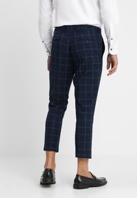 Marineblaue, kariertes Slim-Fit-Hosen mit zwei Gesäßtaschen und knöchellangen Säumen. Hergestellt aus leichtem Stoff.