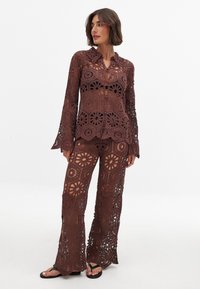 Brown crochet set featuring a long-sleeve button-up top and flared pants, showcasing intricate circular patterns and cut-out details.