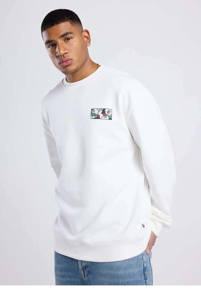 Sweatshirt blanc à manches longues, col ras du cou, avec une petite écusson graphique coloré sur la poitrine. Matière en coton, coupe décontractée.