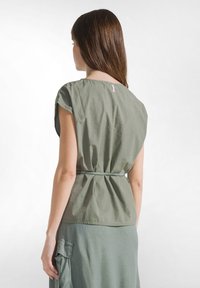 Groene katoenen blouse met korte mouwen, getailleerde taille, zachte textuur en een subtiel label bij de halslijn. Heeft een ontspannen pasvorm.