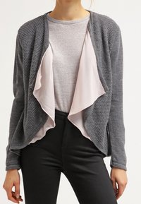 Cardigan grigio lavorato a maglia con uno strato interno in satin rosa, design aperto sul davanti, maniche lunghe e superficie testurizzata. Abbinato a una t-shirt grigia.