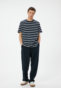 Marineblå og hvidstribet bomuld T-shirt med korte ærmer, parret med løstsiddende marineblå bukser og lyse sneakers. Minimalistisk design.